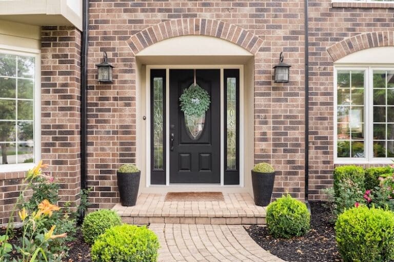 black entry door with two wall lights and two small potted plants